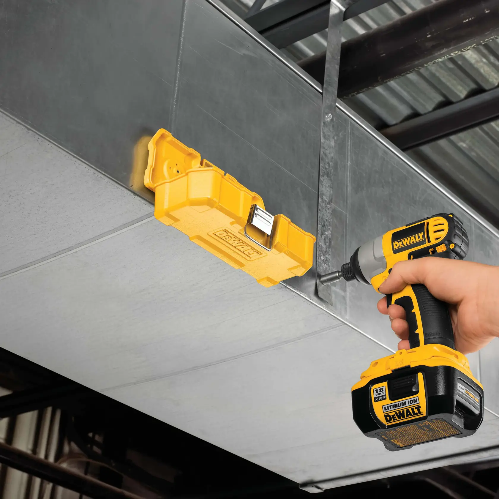 Uma pessoa usa uma furadeira sem fio amarela DEWALT para prender uma caixa de ferramentas amarela DEWALT em um duto ou superfície de metal. O ambiente parece ser industrial ou de construção.