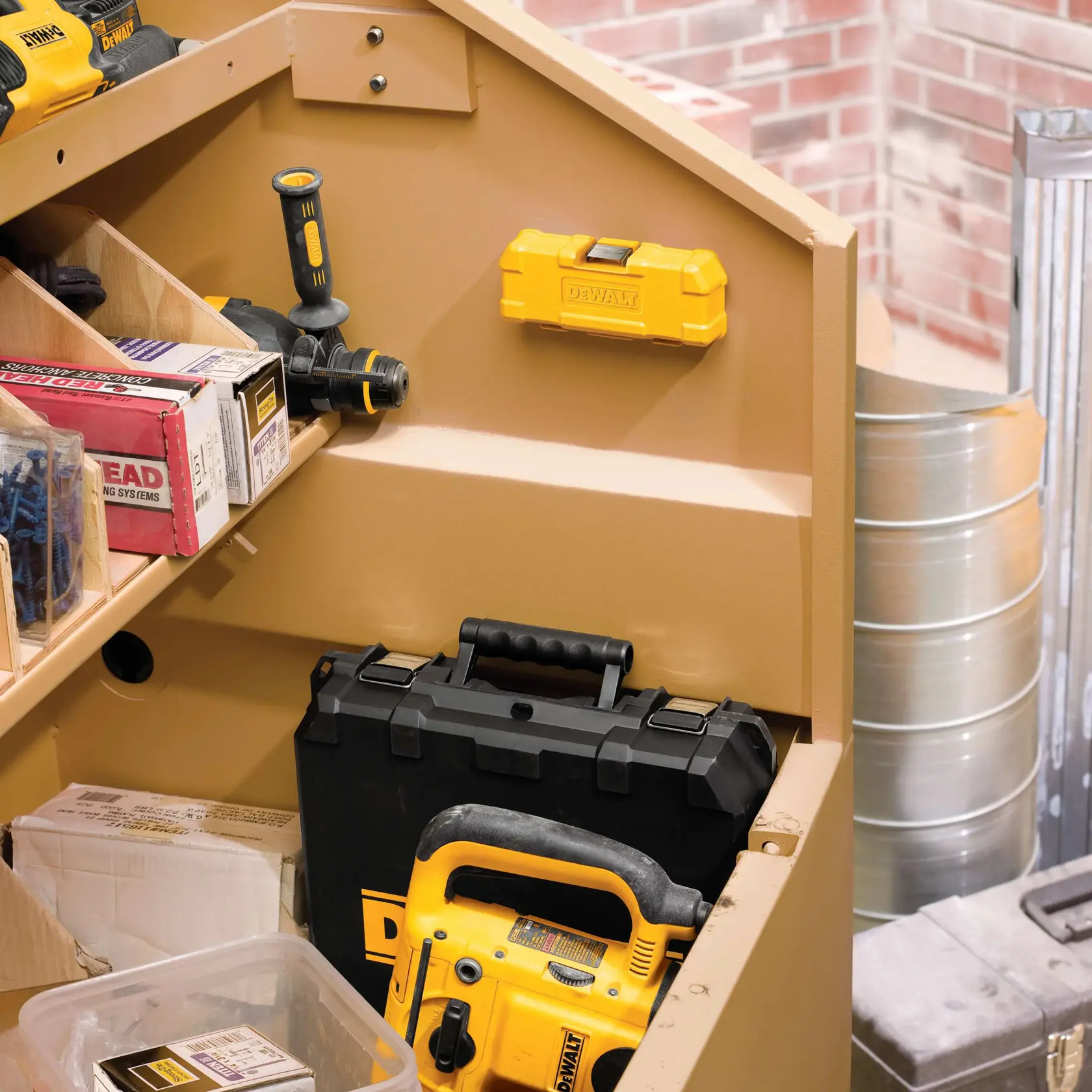 Vista de perto de um armário de armazenamento bege cheio de várias ferramentas e equipamentos DEWALT, incluindo uma furadeira amarela, uma maleta de ferramentas preta e amarela, uma caixa de ferramentas amarela fixada na parede e diversas caixas e recipientes. A cena está localizada em uma oficina, com uma parede de tijolos e tambores de metal ao fundo.