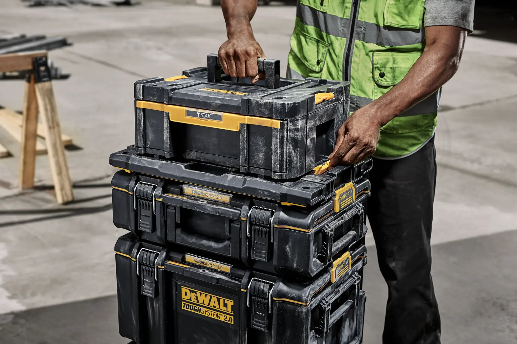 Uma pessoa com colete de segurança empilha caixas de ferramentas DEWALT ToughSystem 2.0 e coloca conjuntos ToughCase+ em cima. O texto informa que essas caixas são compatíveis com conjuntos ToughCase+ e sugere adicioná-los à solução de armazenamento ToughSystem 2.0.