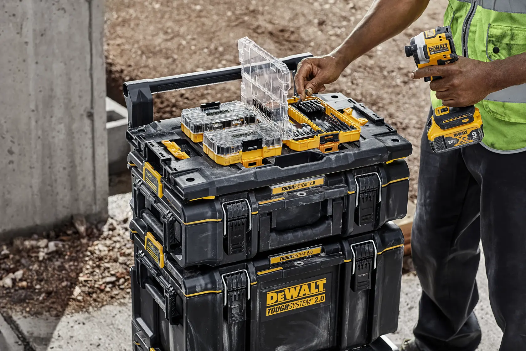 Uma pessoa conecta uma caixa de ferramentas DEWALT TSTAK a uma pilha de módulos de armazenamento ToughSystem 2.0. O texto na imagem diz: 'Compatível com TSTAK. Conecte seus módulos TSTAK existentes a qualquer módulo de armazenamento ToughSystem 2.0 (unidades TSTAK e ToughSystem 2.0 vendidas separadamente)'.