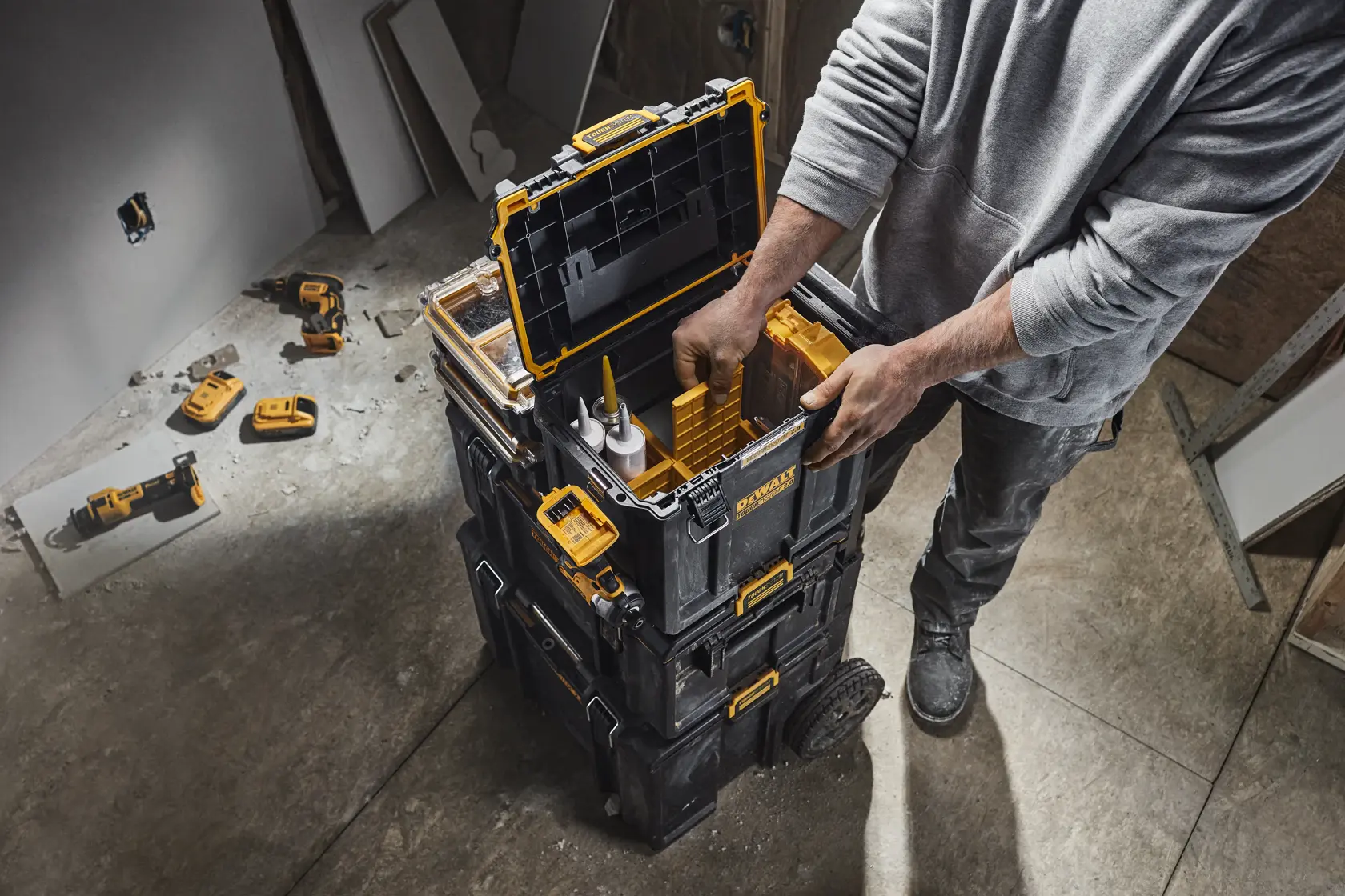 Uma caixa de armazenamento DEWALT ToughSystem 2.0 preta e amarela com a tampa aberta, contendo ferramentas elétricas e acessórios. A caixa possui alças laterais com ranhuras para pendurar ferramentas elétricas e acessórios. O texto na imagem destaca a capacidade de armazenamento adicional e a funcionalidade.