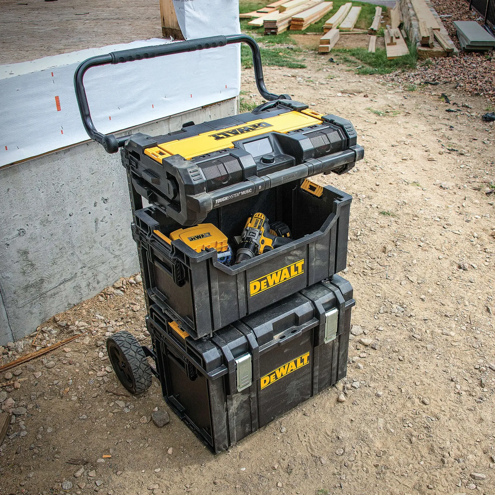Caixas de ferramentas DEWALT empilhadas com alça e rodas, posicionadas ao ar livre em um local de construção, parcialmente abertas mostrando ferramentas elétricas dentro.