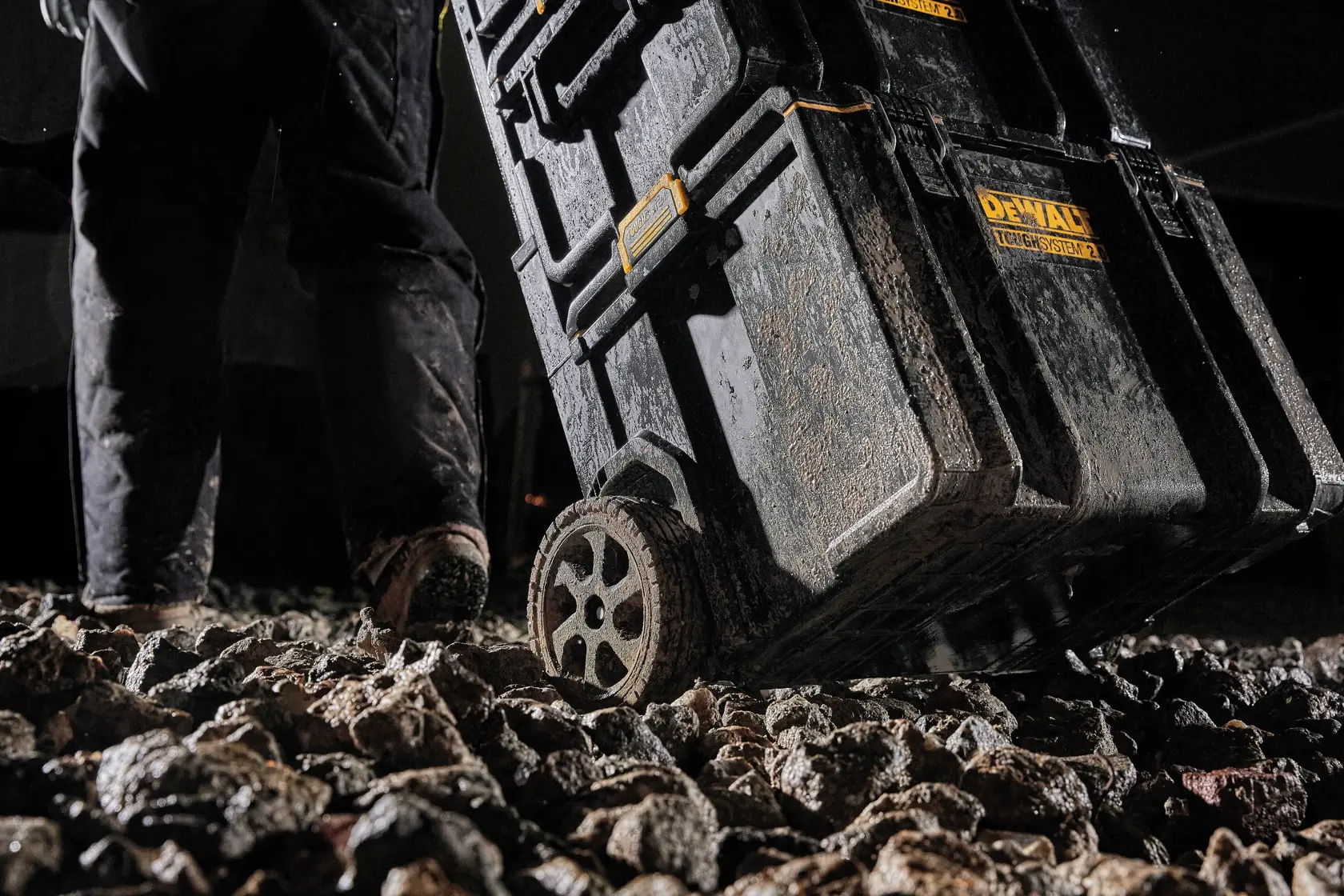 Close-up de uma caixa de armazenamento de ferramentas DEWALT ToughSystem sendo transportada em um terreno rochoso, destacando suas rodas todo-terreno de 8 polegadas.