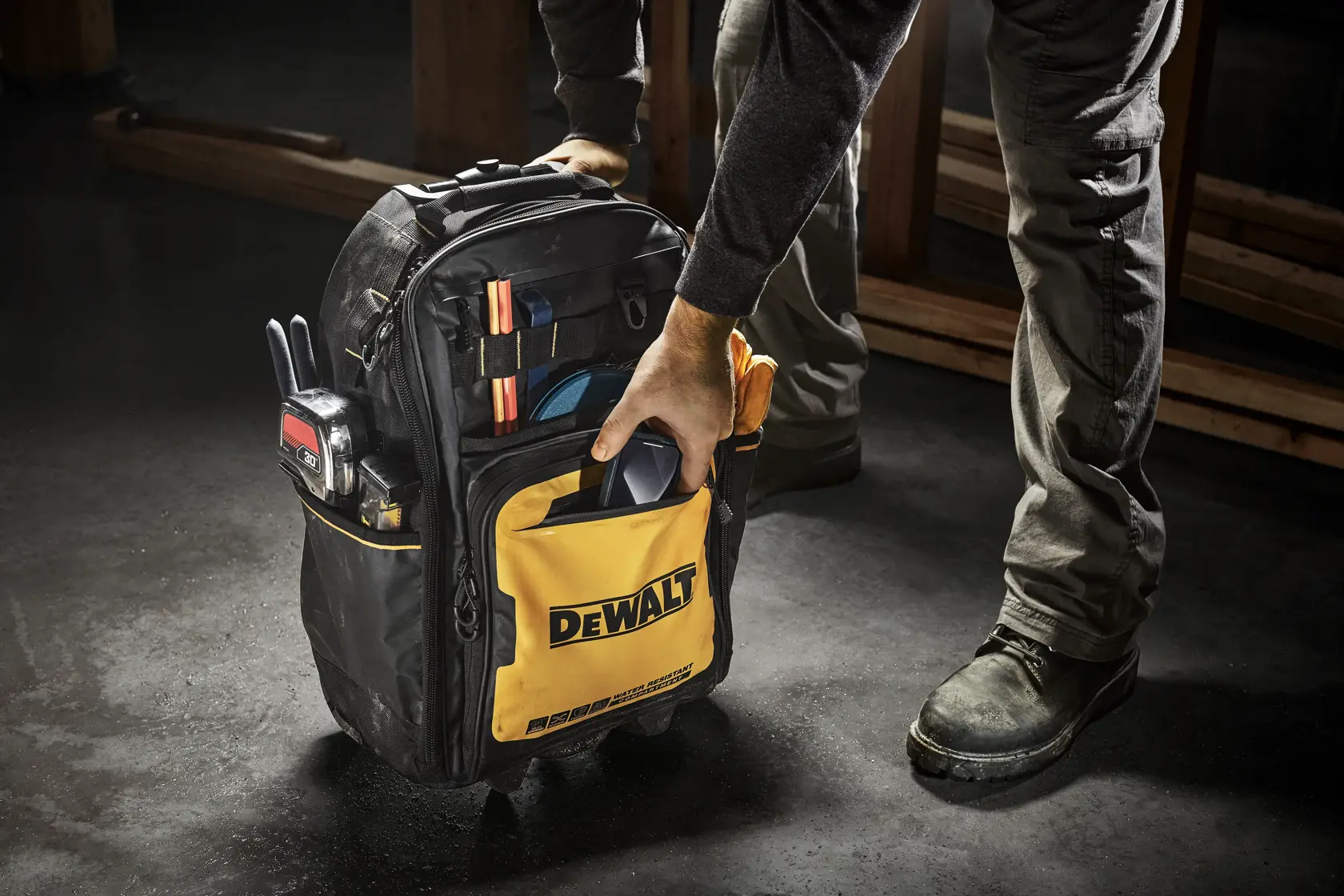 Se muestra una mochila para herramientas DEWALT negra y amarilla con el compartimento delantero abierto, mostrando varios bolsillos y bucles organizados para guardar herramientas y equipos.