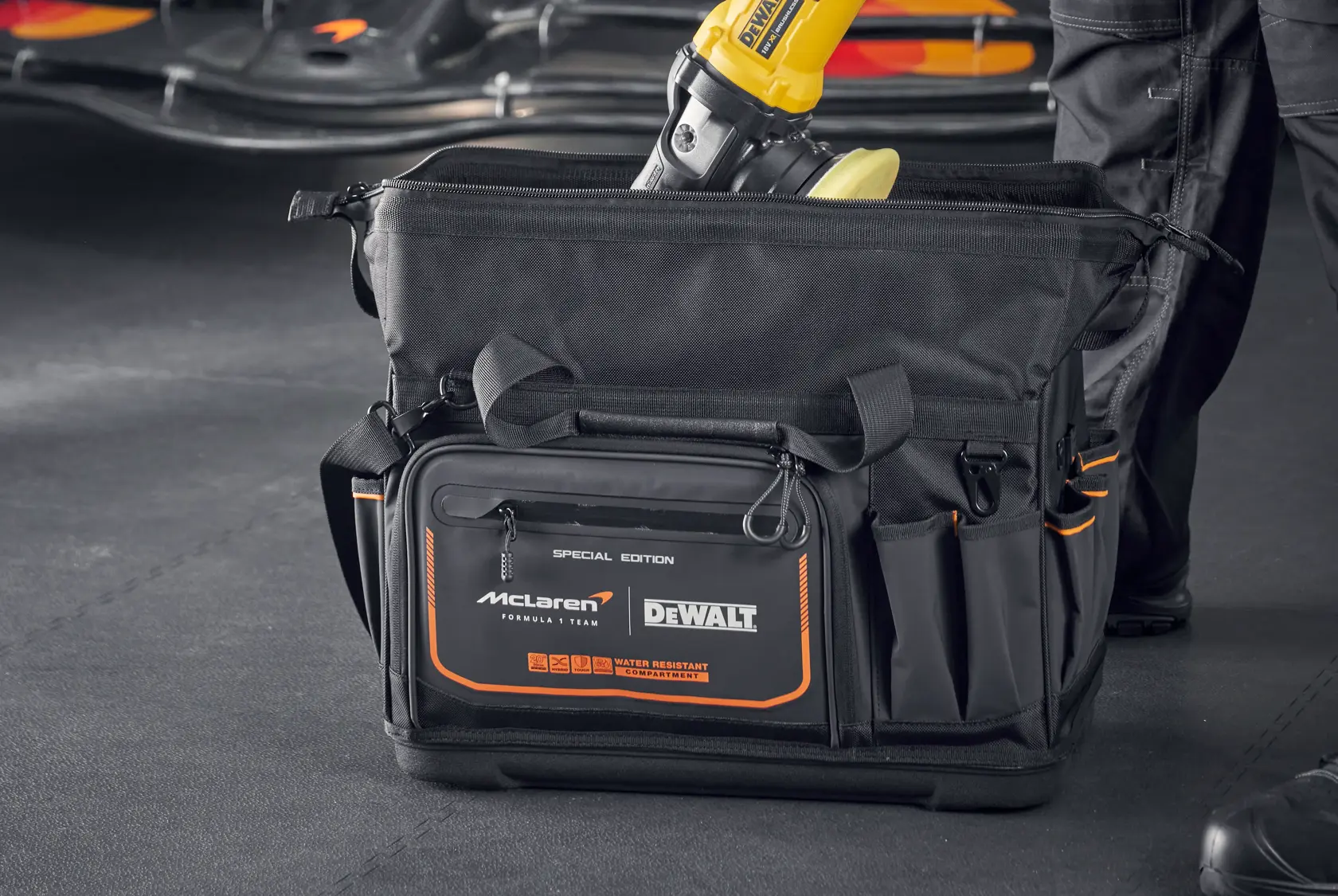 Bolsa de ferramentas DEWALT McLaren preta com detalhes laranja e compartimentos, mostrada em oficina.