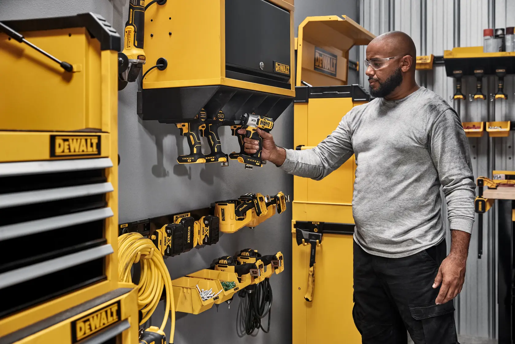Imagem mostrando duas caixas de armazenamento amarelas DEWALT. Inclui etiquetas destacando características principais: montagem sem ferramentas nos trilhos metálicos DEWALT, acesso rápido ao conteúdo com abertura frontal grande, sistema de armazenamento personalizável para oficina, capacidade máxima de carga de 10 libras por caixa, organização otimizada para pequenos itens e acessórios, e construção durável com plástico composto resistente.